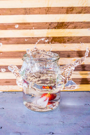 A piece of ice fell into a glass with a transparent cocktail and a splash occurred from the edges of...
