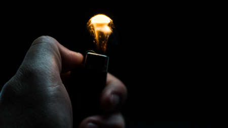 A person has lighters in his hands and he lights it through a flint wheel, the lighter ignites, sparks and fire appear, close-up on a black background.の写真素材