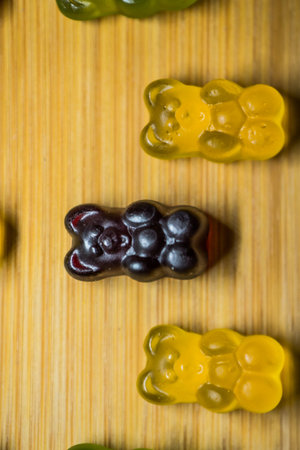 Many gummy bears of different colors and flavors on a wooden background.