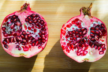 A juicy large pomegranate is cut into two parts and lies on a wooden table.の写真素材