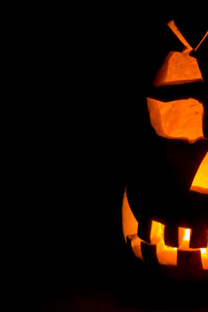 Half of an evil pumpkin close-up glowing in a dark room.の写真素材
