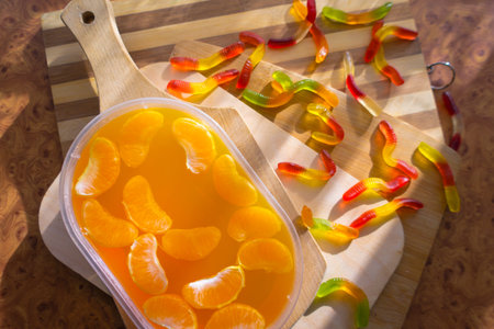 Orange jelly in a plastic container with tangerine slices on wooden planks.