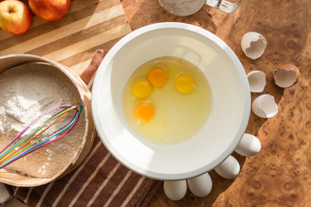 Eggs hammered into a white bowl for a delicious and airy sponge cake with apples.