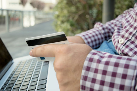 man holding credit card and laptop staying outside and paying or buying online, self-employed,...