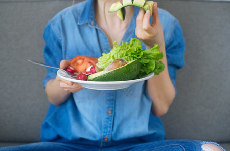 young woman eating fresh vegetables at home. Vegan eating avocado, salad, radish and tomatos