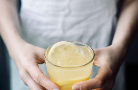 a woman drinking lemonade at home, woman keeping in hands a glass of refreshing drink with lemon and iceの写真素材