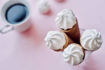 waffle sweet cone with white sweets meringue with cup of coffee over pastel light pink background, top view. Spring mood concept, birthday, breakfast or tasty treatの写真素材