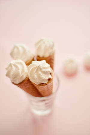 waffle sweet cone with white sweets meringue over pastel light pink background, top view. Spring mood concept, birthday, breakfast or tasty treatの写真素材