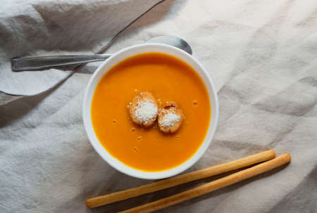 Flat-lay of fall warming pumpkin cream soup with croutons over tablecloth background Autumn vegetarian, vegan, healthy comfort food eating conceptの写真素材