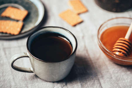 Hot tea with biscuits cookies and honey in cup over tableclothの写真素材