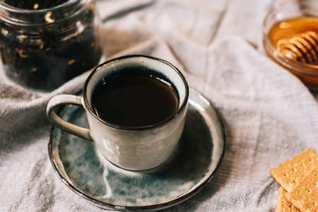 Cup of hot winter drink tea leaves biscuits cookies and honey in cup over tableclothの写真素材