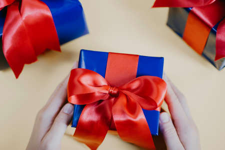 flat-lay of woman hands holding present box with red bow ribbon on pastel yellow background. Christmas new year or birthday gift boxの写真素材