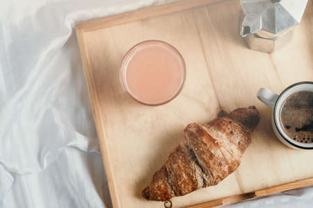 Breakfast in bed on white silky linen. Croissant, coffee and juice Window lightの写真素材