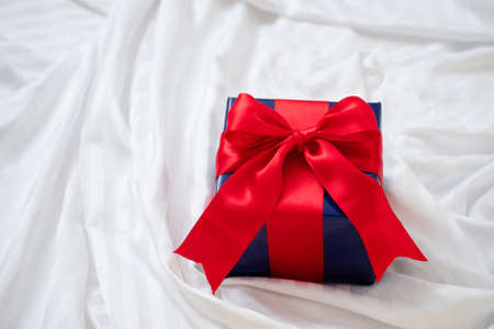 gift box with red ribbon on white silky sheet on bed, romantic valentine's conceptの写真素材