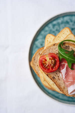 Tasty fresh pieces of bread with ham tomatoes and rocket salad on plat over white backgroundの写真素材