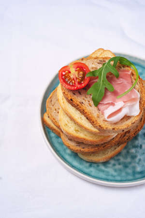 side view Tasty fresh pieces of bread with ham tomatoes and rocket salad on plat over white backgroundの写真素材