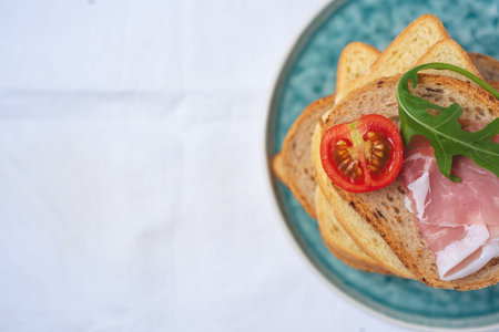 copy space, flat lay of Tasty fresh pieces of bread with ham tomatoes and rocket salad on plat over white backgroundの写真素材