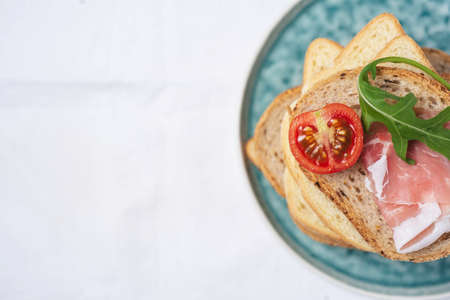 copy space, flat lay of Tasty fresh pieces of bread with ham tomatoes and rocket salad on plat over white backgroundの写真素材