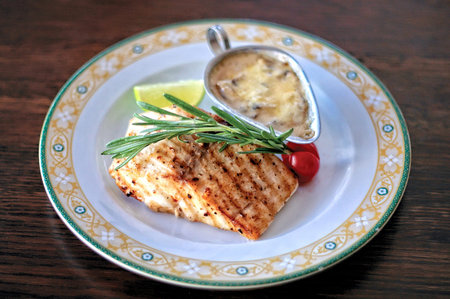 A plate of grilled escolar fish with creamy sauce on a rustic wooden table.