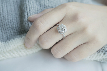 Close up Diamond ring on woman's finger before wedding with white and gray scarf background.soft sunlight tone(soft and selective focus)Close up of elegant diamond ring on the finger with gray Scarfの写真素材