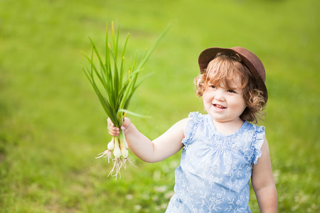 Adorable little girl with onion in the gardenの写真素材