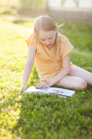 Blonde teenager girl doing her summer homework in the backyard, learning and reading. beautiful natural lightの写真素材