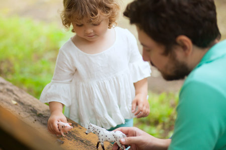 Cute toddler girl playing with her father outdoors. farm animal figures. Summer leisure. childhood...