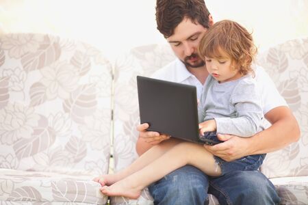 Little girl sitting on fathers knees looks at the laptop with serious pensive face. Child working with device. Early education, early developement. Wunderkind concept. Smart kid. Kids and technology. Caring loving father Child and technology. Copyspace, eの写真素材