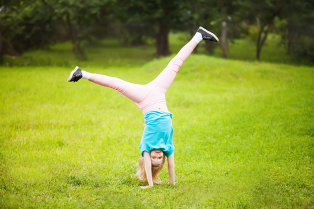 Cute athletic school girl tumbling, turning, turn handsprings in the park.の写真素材