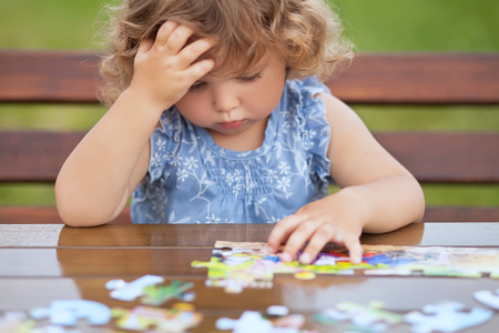 blonde unhappy toddler girl, solving puzzle on a table, hard difficult task. Early education and developement. Little genius concept. Emotional.の写真素材