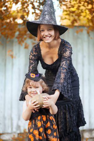 Mother and her little daughter ready for trick or treat, wearing halloween witch costumes. Autumn day outdoors, yellow leavesの写真素材