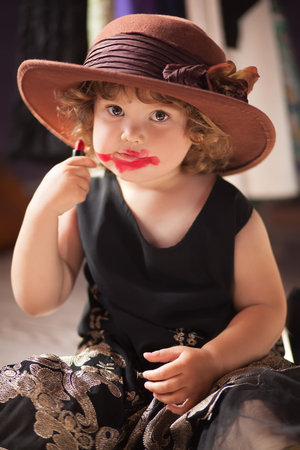 Little girl wearing mothers clothing evening dress and felt hat, 	
making make up with mother cosmetics. Learning to be a womanの写真素材