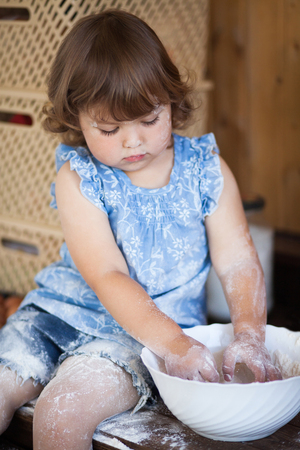 Cute toddler smiling kid in the rustic kitchen indoors. Baking sweet apple cake and having fun. Flour dirty hands. Homemade food.の写真素材