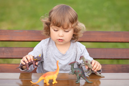 little girl having fun playing with a toy dinosaur plastic figurine, horizontal natural light photo. Child studying dinosaursの写真素材