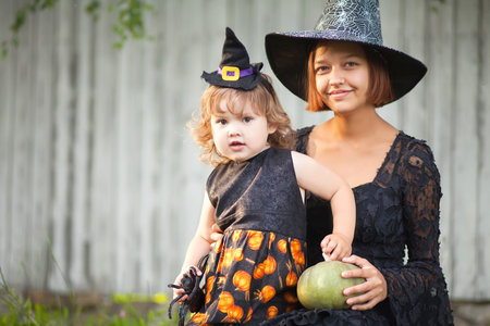 Mother and her little daughter ready for trick or treat, wearing halloween witch costumes. Fall day...