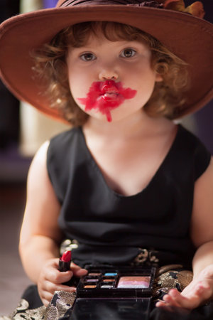 Little girl wearing mothers clothing evening dress and felt hat, 	
making make up with mother...