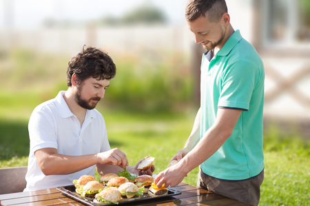 Two men friends outdoor, preparing fast food hamburgers, warm summer day, party.の写真素材