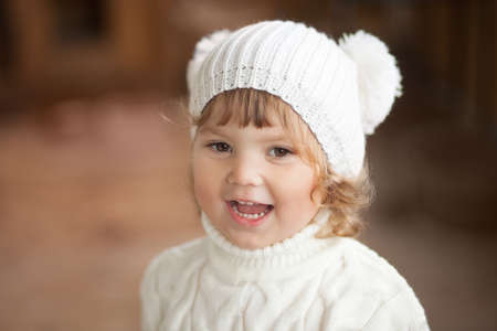 Adorable happy little girl wearing white knitted hat and scarf, autumn day.の写真素材