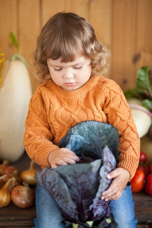 Cute happy little kid with different vegetable harvest, autumn, wood background, countryside, family farmの写真素材
