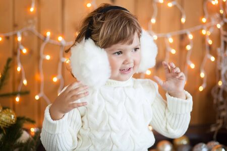 Cute little girl wearing white knitted sweater, smiling, christmas decorations on a backgroundの写真素材