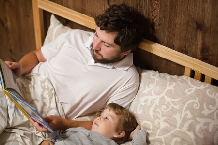Family night, handsome caring father reading a book to his cute little daughter before bedの写真素材