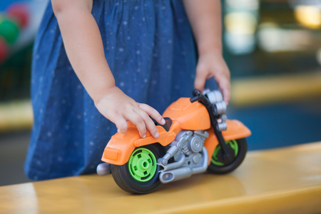 Cute happy toddler girl playing with boys toys on a playground or kindergartenの写真素材