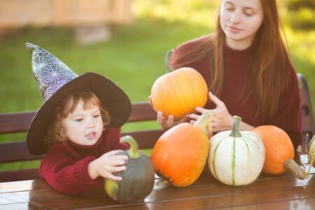 Happy family preparing for Halloween, choosing pumpkins outdoors. Fall day, warm toned photoの写真素材