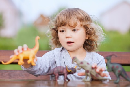 little girl having fun playing with plastic dinosaurs outdoorsの写真素材