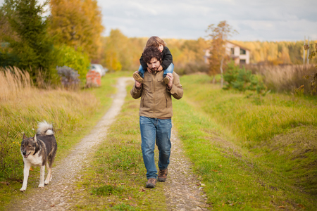 Father and daughter walking with dog together in the park, fall day. Little girl and her dad exploring nature outdoors. Colorful autumn foliage. Copyspace.の写真素材
