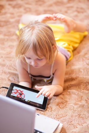 Little girl playing computer game indoors, using tablet and laptop, kids and technologyの写真素材