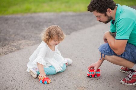 Father play with his toddler daughter in boys games. Two color cars. Family leisure. Loving caring single father. Kid playing with parent.の写真素材