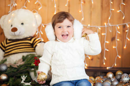 Cute little girl wearing white knitted sweater, smiling, christmas decorations on a backgroundの写真素材
