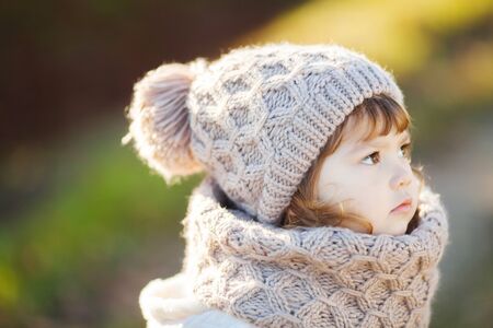 Autumn outdoor portrait of happy child girl, wearing warm white coat, scarf and hat, photoの写真素材