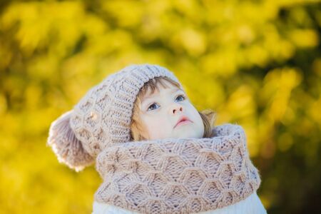 Autumn outdoor portrait of happy child girl, wearing warm white coat, scarf and hat, photoの写真素材